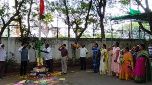 Officials and staff members standing in salute during the Indian National Flag hoisting ceremony as part of Telangana Formation Day 2026 celebrations on a government office campus.